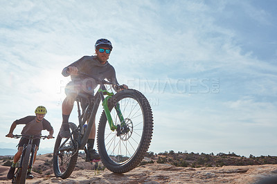 Buy stock photo Full length shot of two athletic men mountain biking through the wilderness