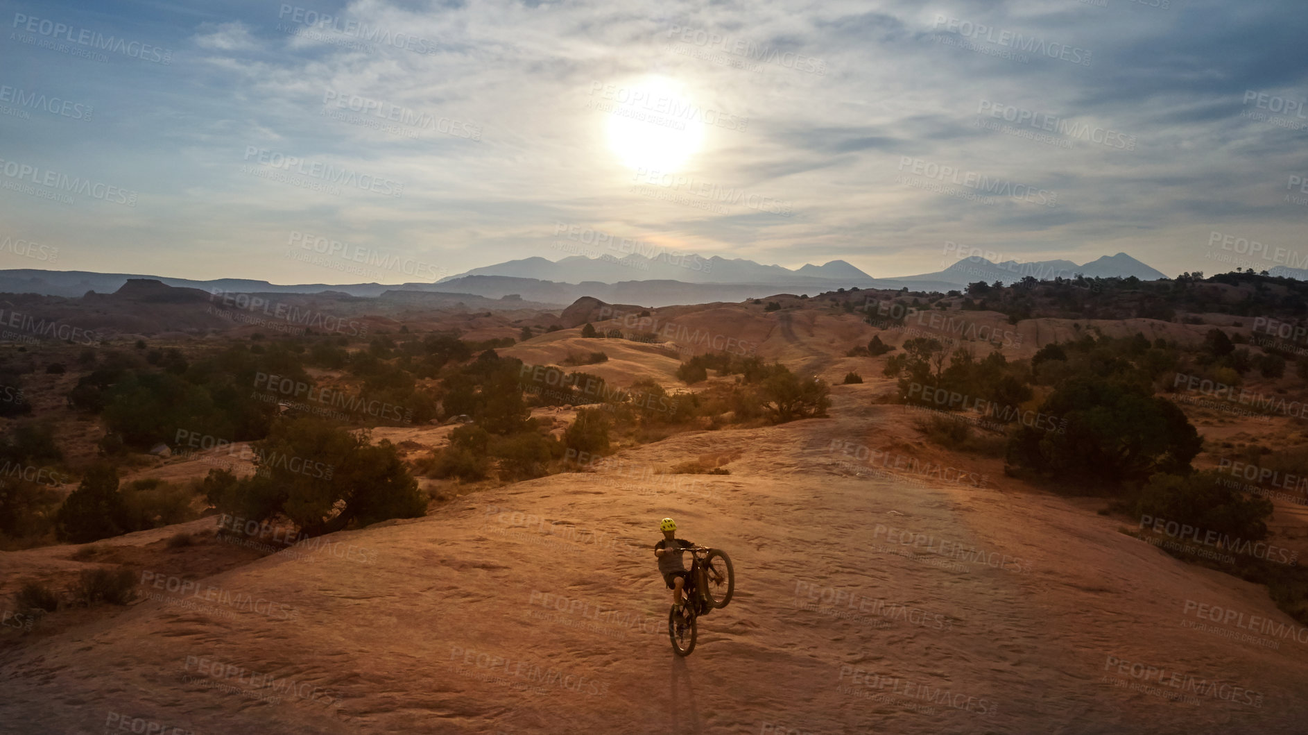 Buy stock photo Full length shot of a young male athlete popping a wheelie while mountain biking in the wilderness