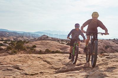 Buy stock photo Full length shot of two athletic men mountain biking through the wilderness