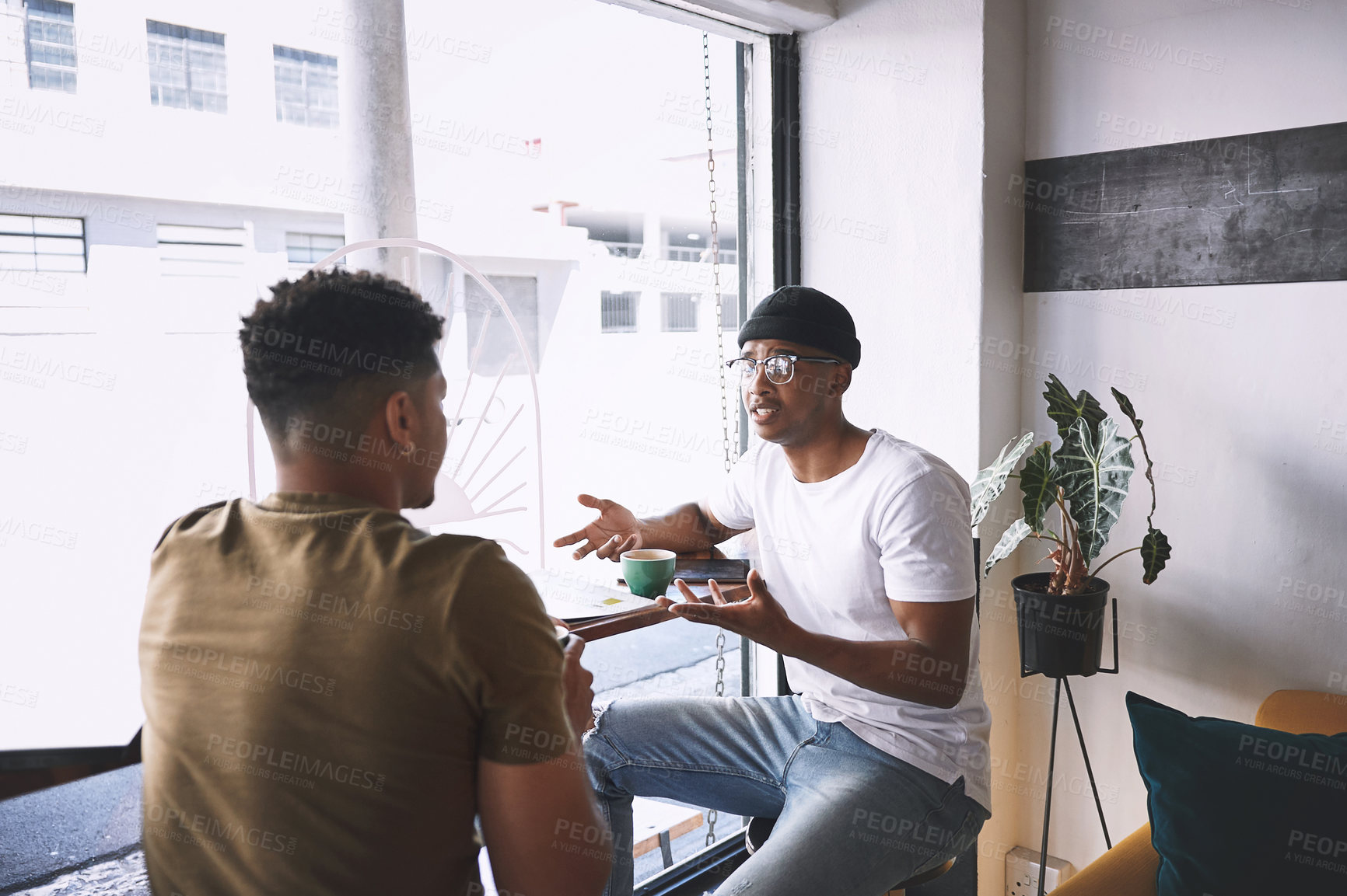 Buy stock photo Shot of two young men talking while having coffee together in a cafe