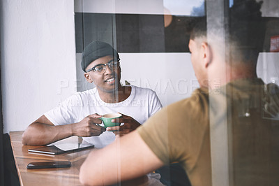 Buy stock photo Shot of two young men talking while having coffee together in a cafe