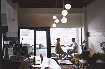 Buy stock photo Shot of two young men talking while having coffee together in a cafe