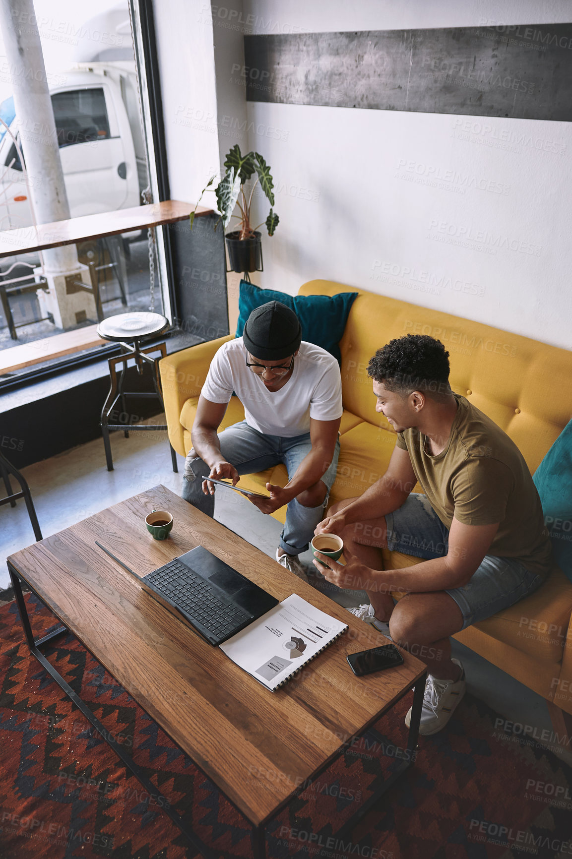 Buy stock photo Shot of two men using a laptop and a digital tablet while having coffee together