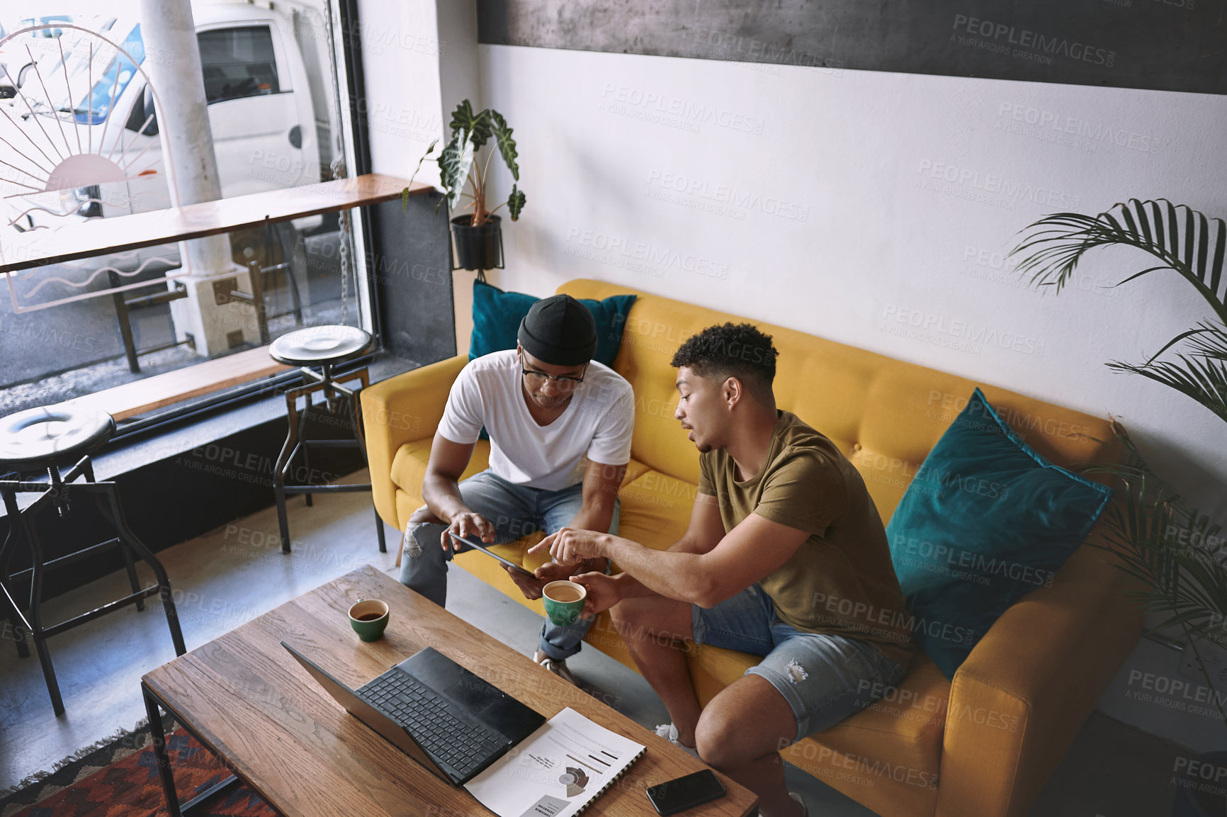 Buy stock photo Shot of two men using a laptop and a digital tablet while having coffee together