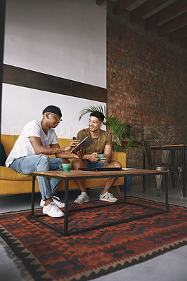 Buy stock photo Shot of two young men using a digital tablet while having coffee together