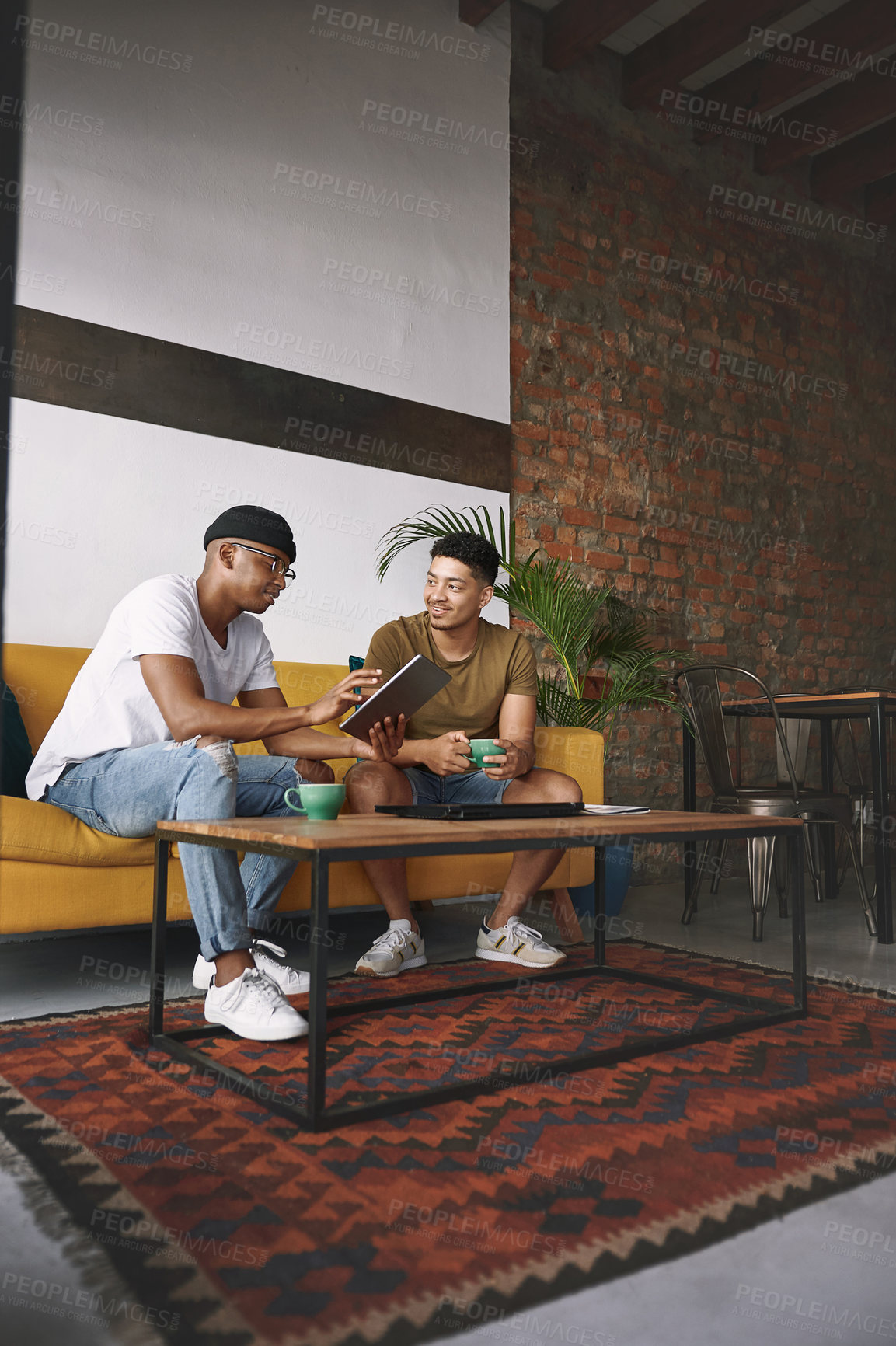 Buy stock photo Shot of two young men using a digital tablet while having coffee together