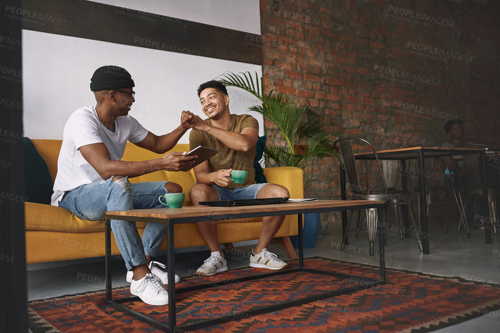 Buy stock photo Shot of two young men sharing a fist bump while sitting in a coffee shop