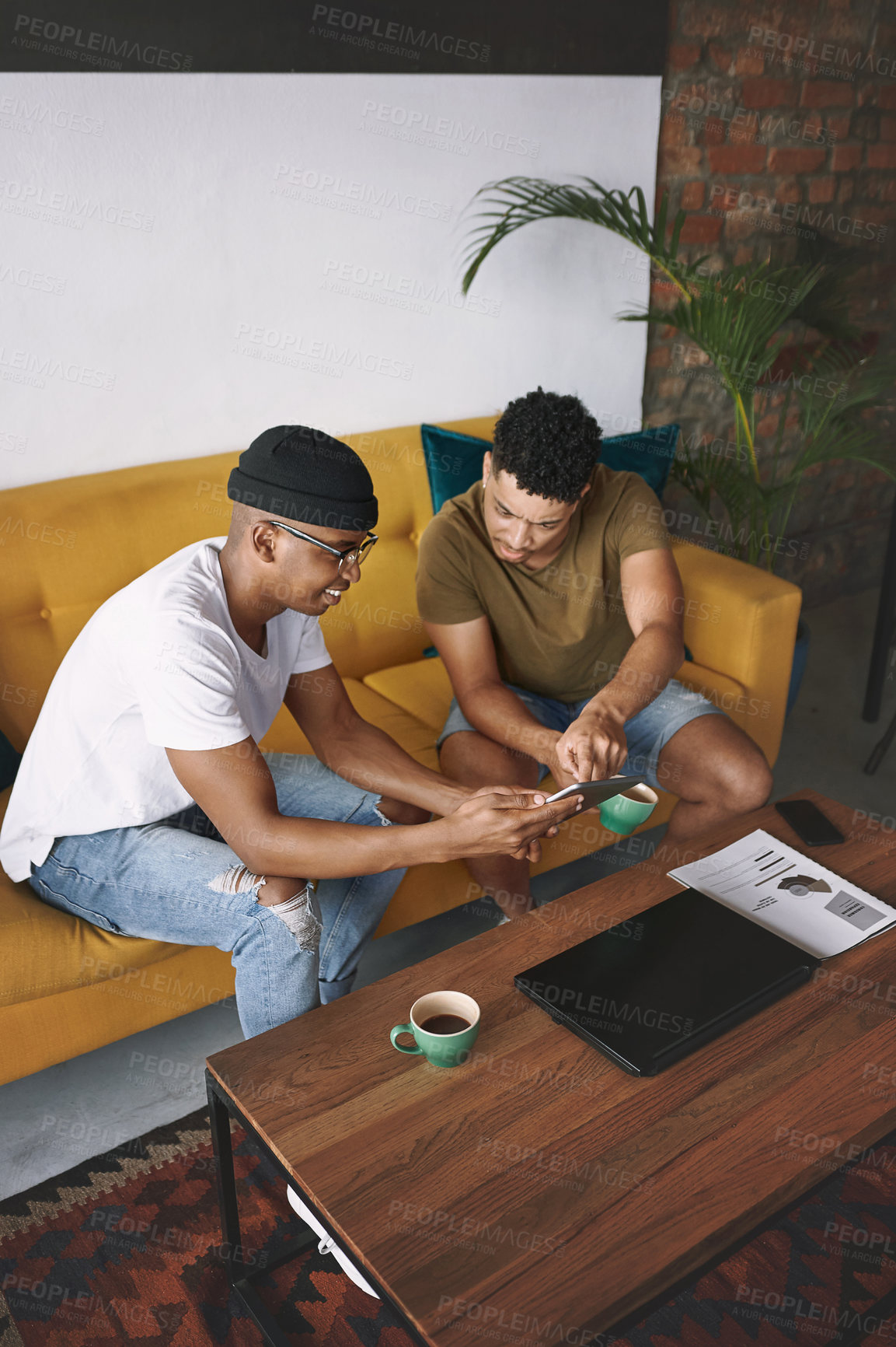 Buy stock photo Shot of two young men using a digital tablet while sitting together in a coffee shop