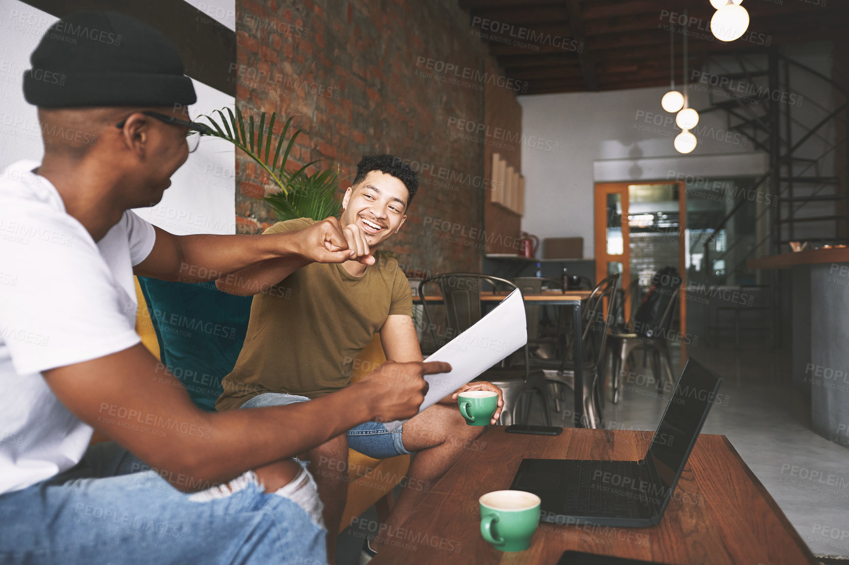 Buy stock photo Shot of two young men sharing a fist bump while sitting in a coffee shop