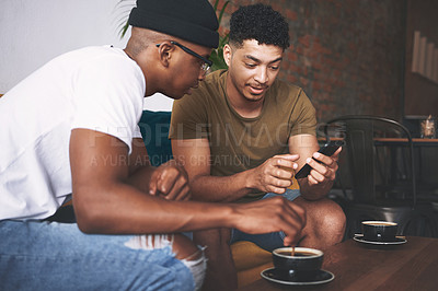 Buy stock photo Shot of men discussing something on a cellphone while sitting together in a coffee shop