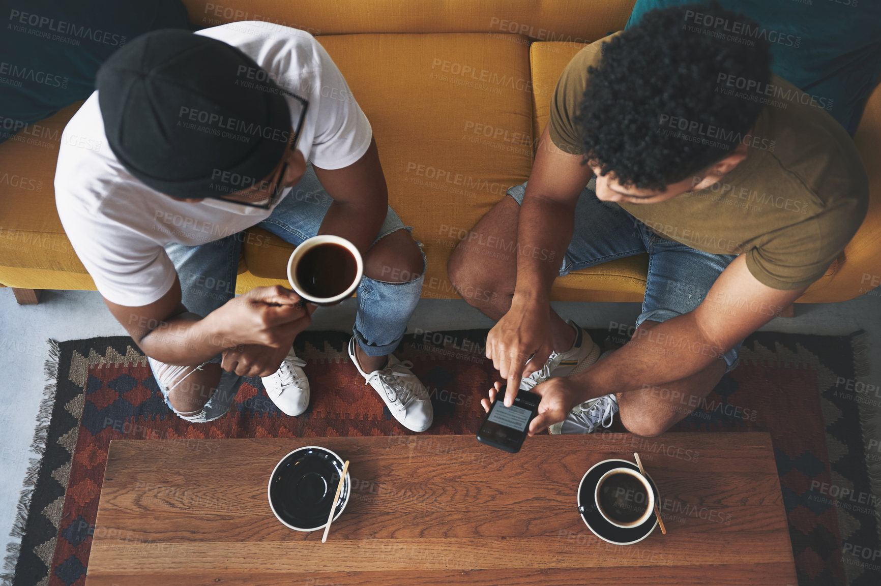 Buy stock photo Shot of men discussing something on a cellphone while sitting together in a coffee shop