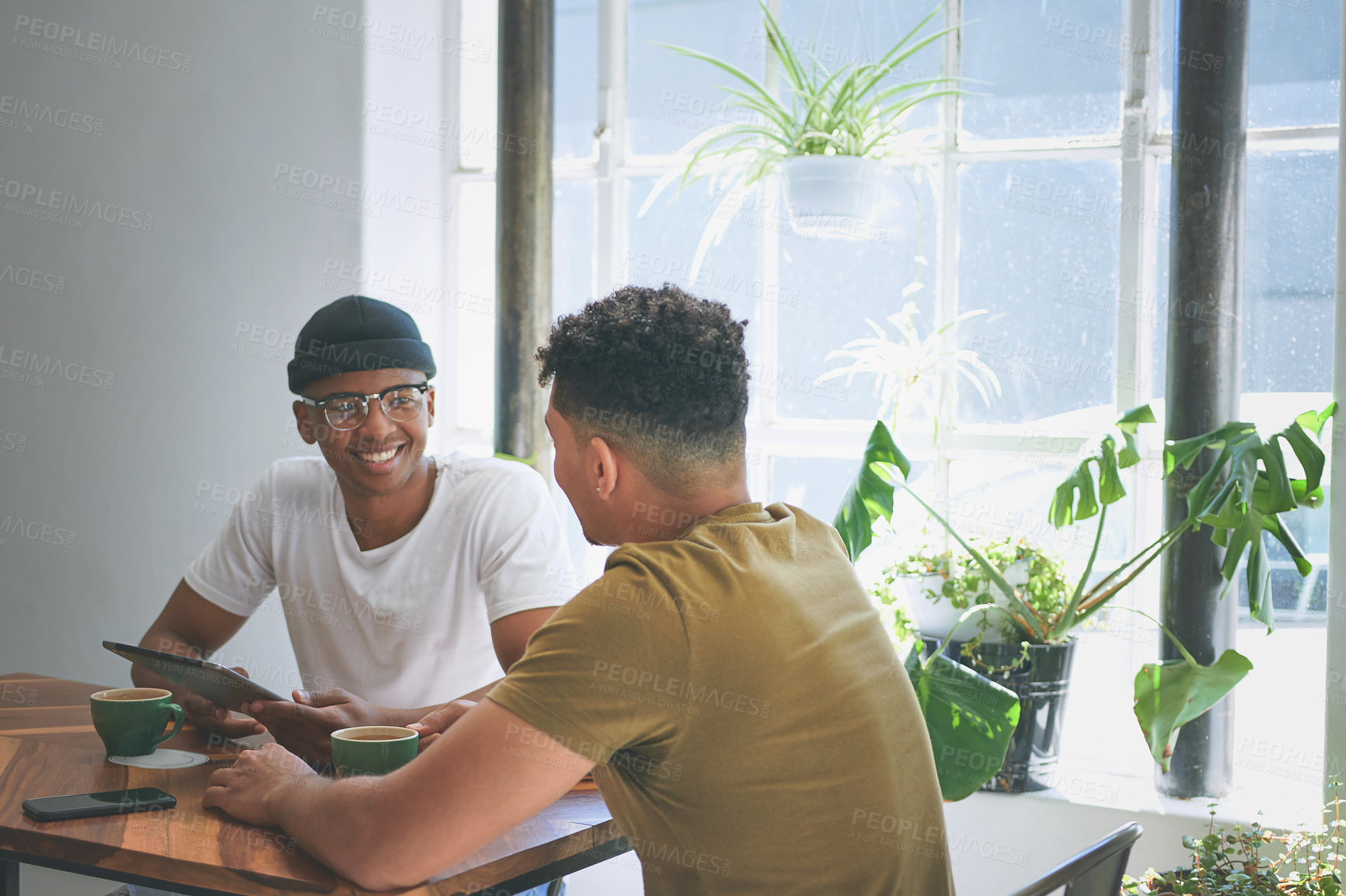 Buy stock photo Cropped shot of two handsome friends sitting together and bonding over a coffee in a cafe during the day