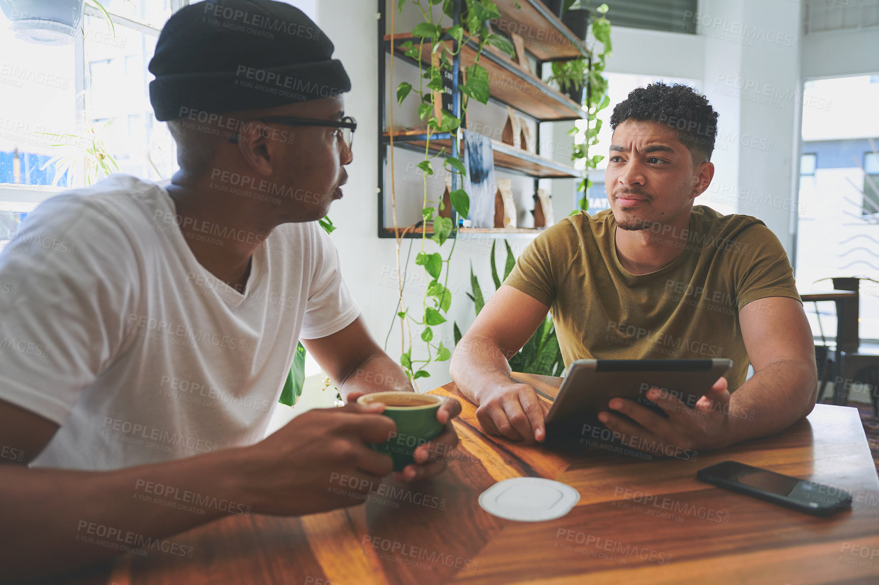 Buy stock photo Cropped shot of two handsome friends sitting together and using a tablet during a discussion in a coffeeshop