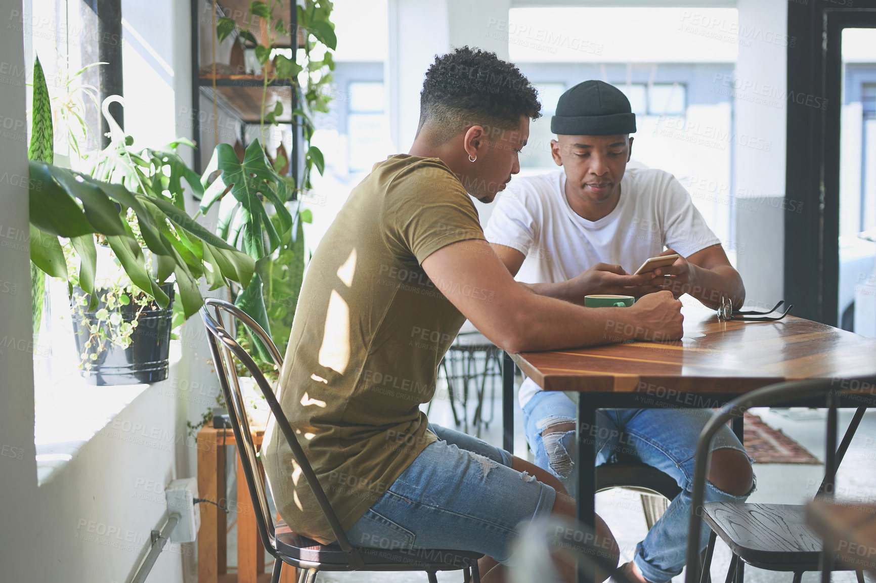 Buy stock photo Cropped shot of two handsome friends sitting together and using a cellphone during a discussion in a coffeeshop