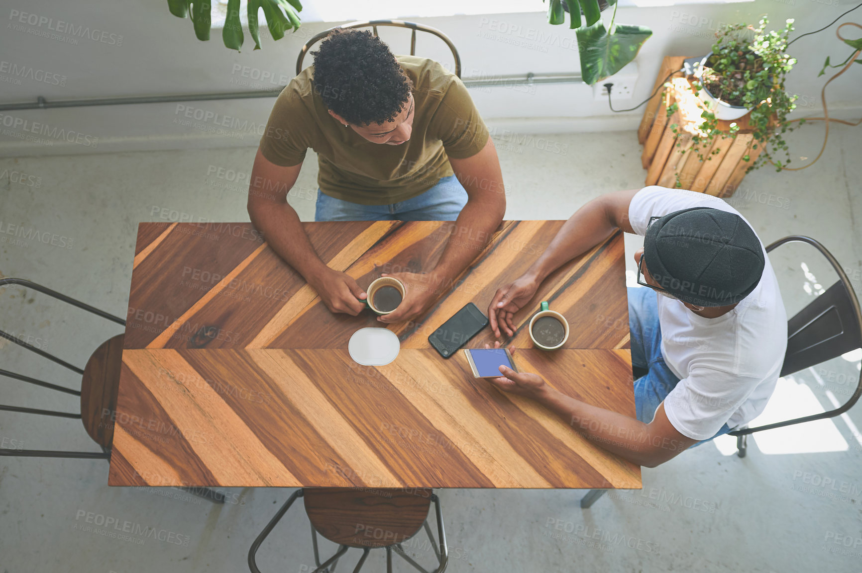 Buy stock photo High angle shot of two unrecognizable friends sitting together and using a cellphone during a discussion in a coffeeshop