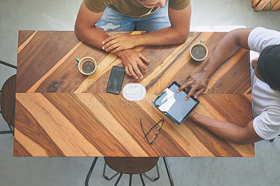Buy stock photo High angle shot of two unrecognizable friends sitting together and using a tablet in a coffeeshop