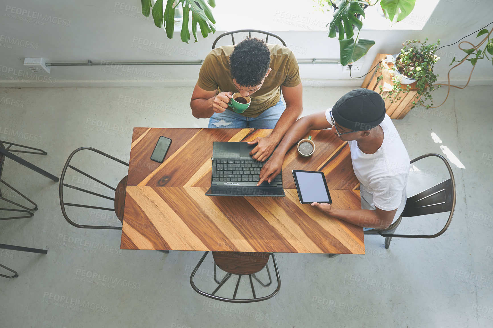 Buy stock photo High angle shot of two friends sitting together and using technology in a coffeeshop