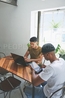 Buy stock photo Cropped shot of two handsome friends sitting together and using technology in a coffeeshop