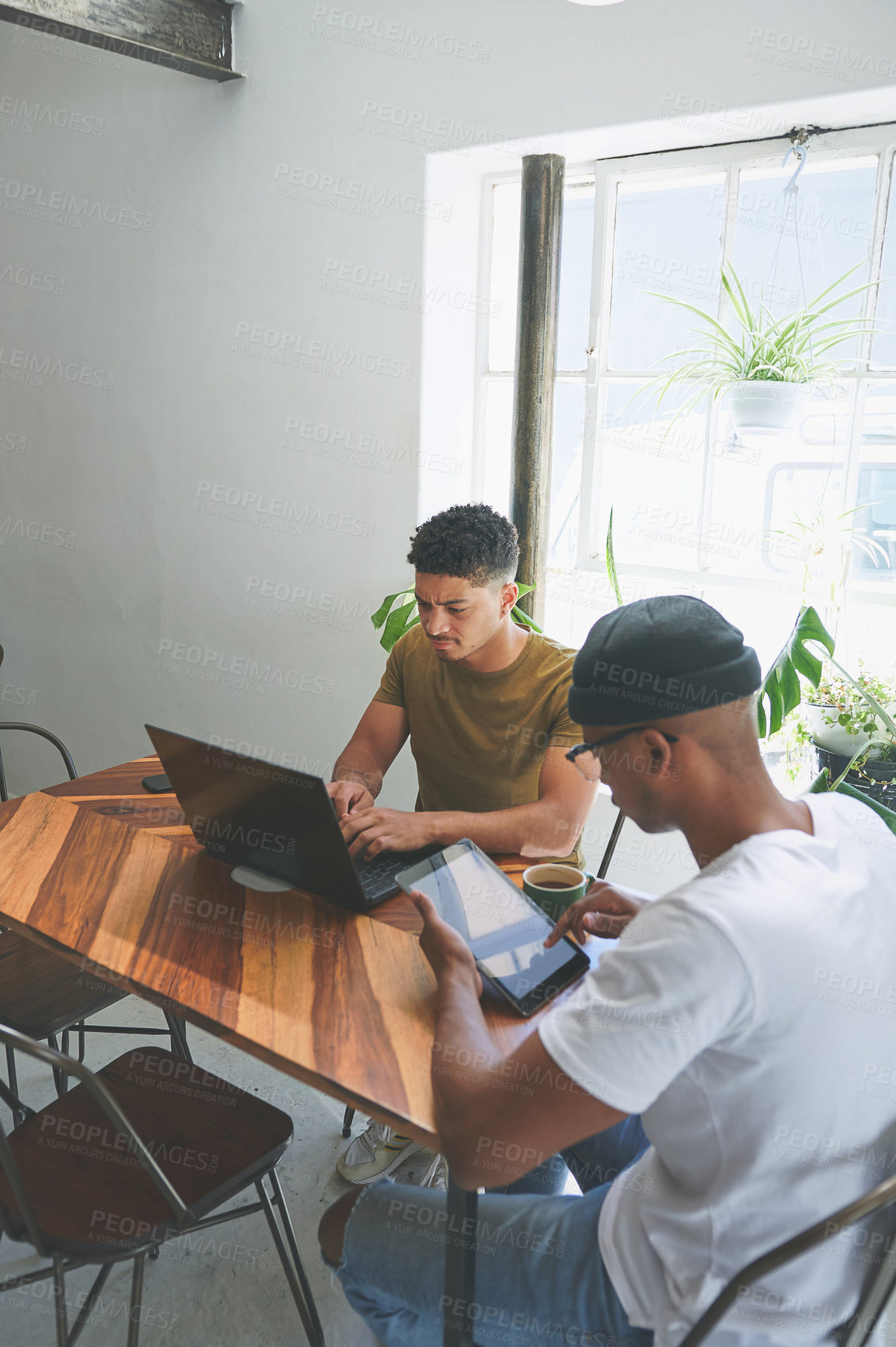 Buy stock photo Cropped shot of two handsome friends sitting together and using technology in a coffeeshop