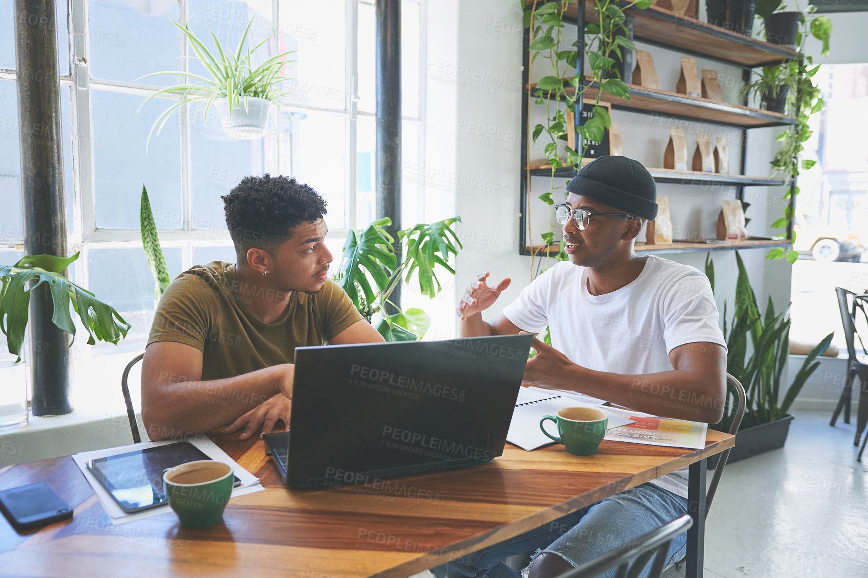 Buy stock photo Cropped shot of two handsome friends sitting together in a coffeeshop and having a discussion