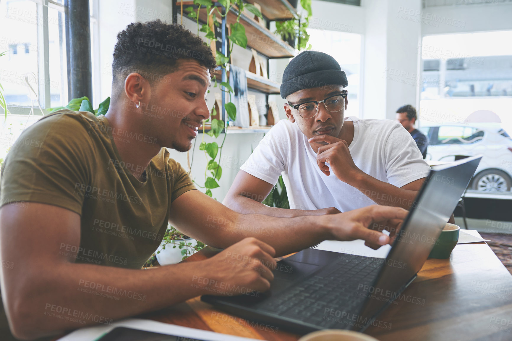 Buy stock photo Cropped shot of two handsome friends sitting together in a coffeeshop and using technology during a discussion