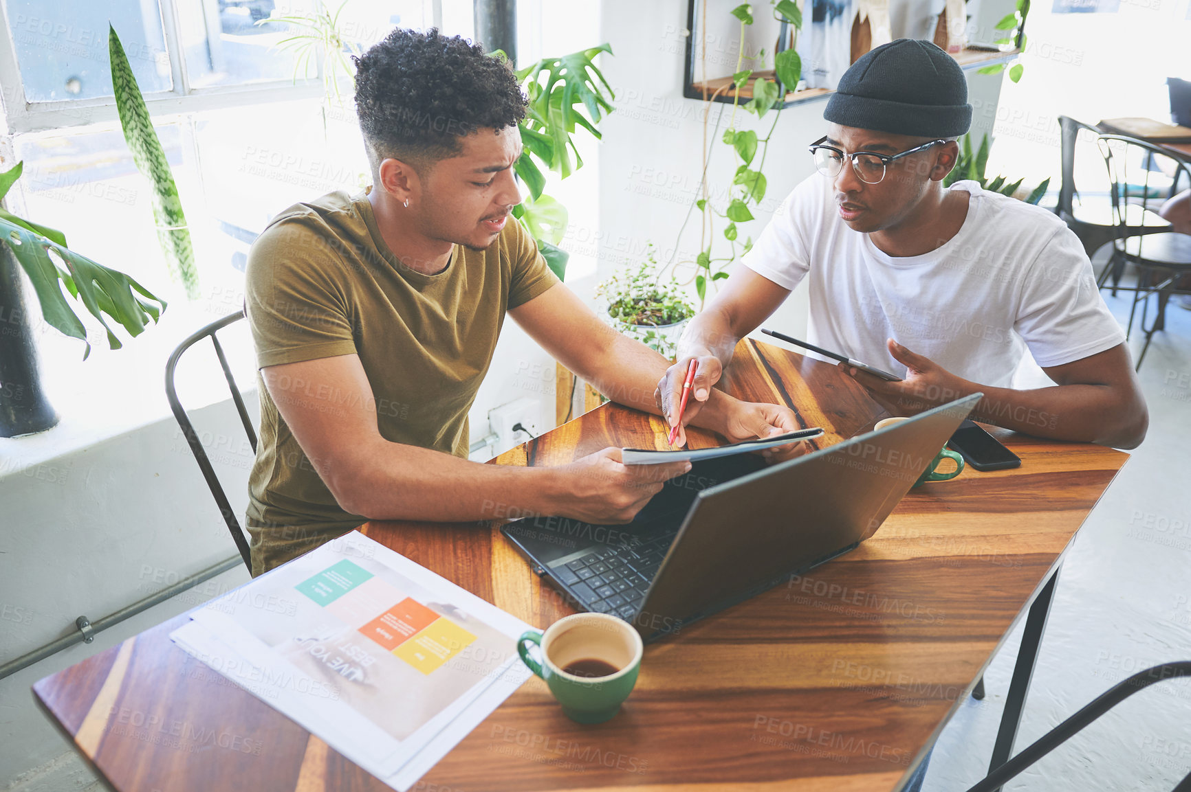 Buy stock photo Cropped shot of two handsome friends sitting together in a coffeeshop and reading through paperwork during a discussion