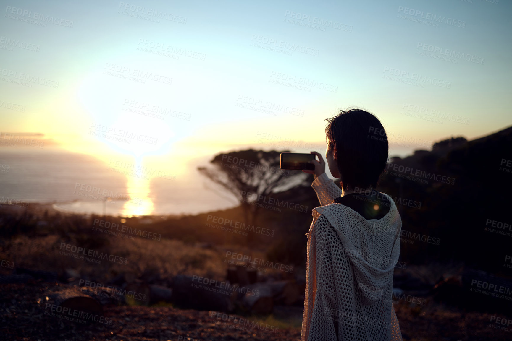 Buy stock photo Shot of a woman taking pictures on her cellphone of the sunset