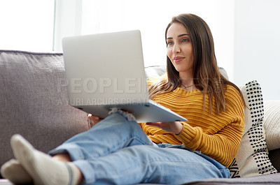Buy stock photo Shot of a young woman using a laptop while relaxing on a sofa at home