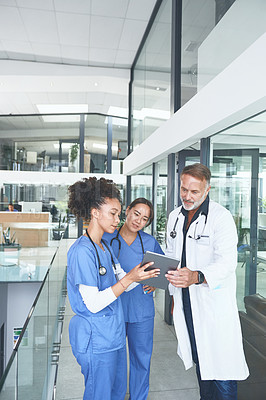 Buy stock photo Cropped shot of a handsome mature doctor standing with his nurses and using a digital tablet during a discussion