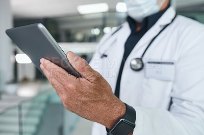 Buy stock photo Cropped shot of a handsome mature doctor standing and wearing a face mask while using a digital tablet
