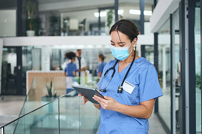 Buy stock photo Cropped shot of an attractive young nurse standing and wearing a face mask while using a digital tablet