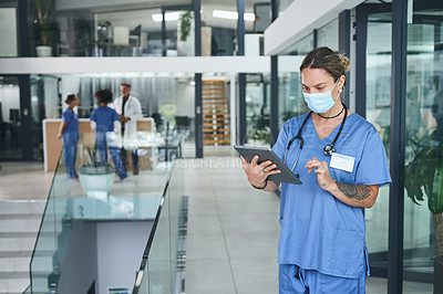 Buy stock photo Cropped shot of an attractive young nurse standing and wearing a face mask while using a digital tablet