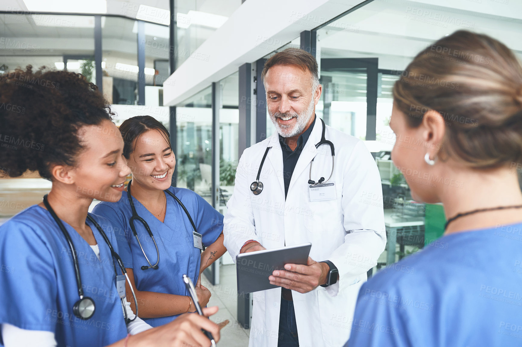 Buy stock photo Cropped shot of a handsome mature doctor standing with his nurses and using a digital tablet during a discussion