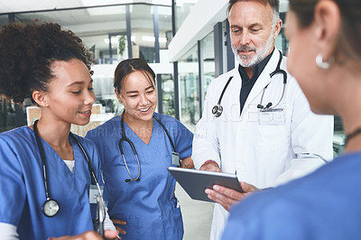 Buy stock photo Cropped shot of a handsome mature doctor standing with his nurses and using a digital tablet during a discussion