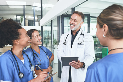 Buy stock photo Cropped shot of a handsome mature doctor standing with his nurses and using a digital tablet during a discussion