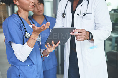 Buy stock photo Cropped shot of an unrecognizable doctor standing with his nurses and using a digital tablet during a discussion