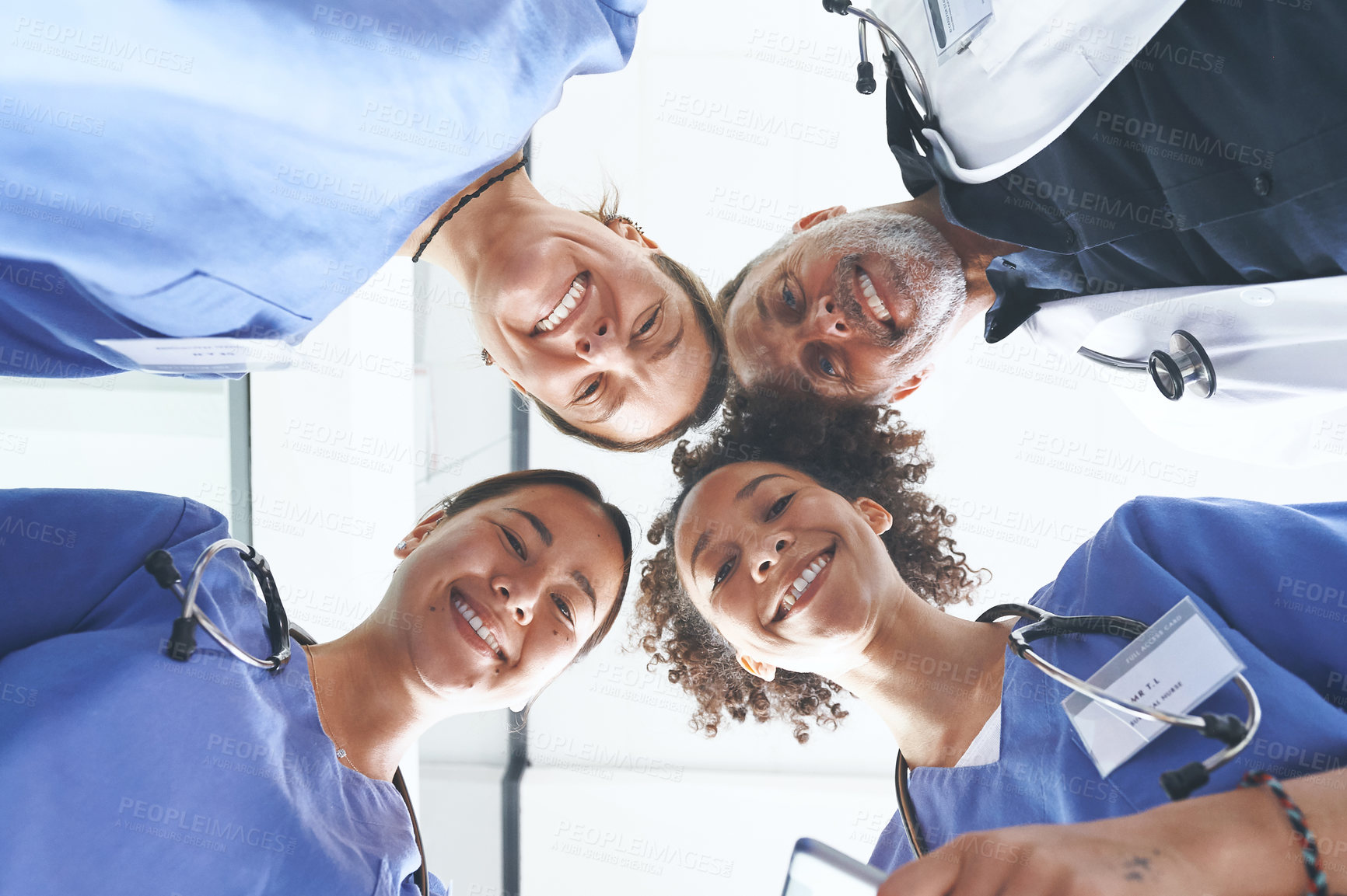 Buy stock photo Low angle portrait of a diverse group of healthcare professionals standing huddled together with their heads together in the middle