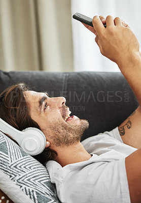 Buy stock photo Man, headphones and phone for sound on couch, relax and listen to song and scroll on social media. Male person, home and rest app for playlist or conversation, text and podcast audio for streaming