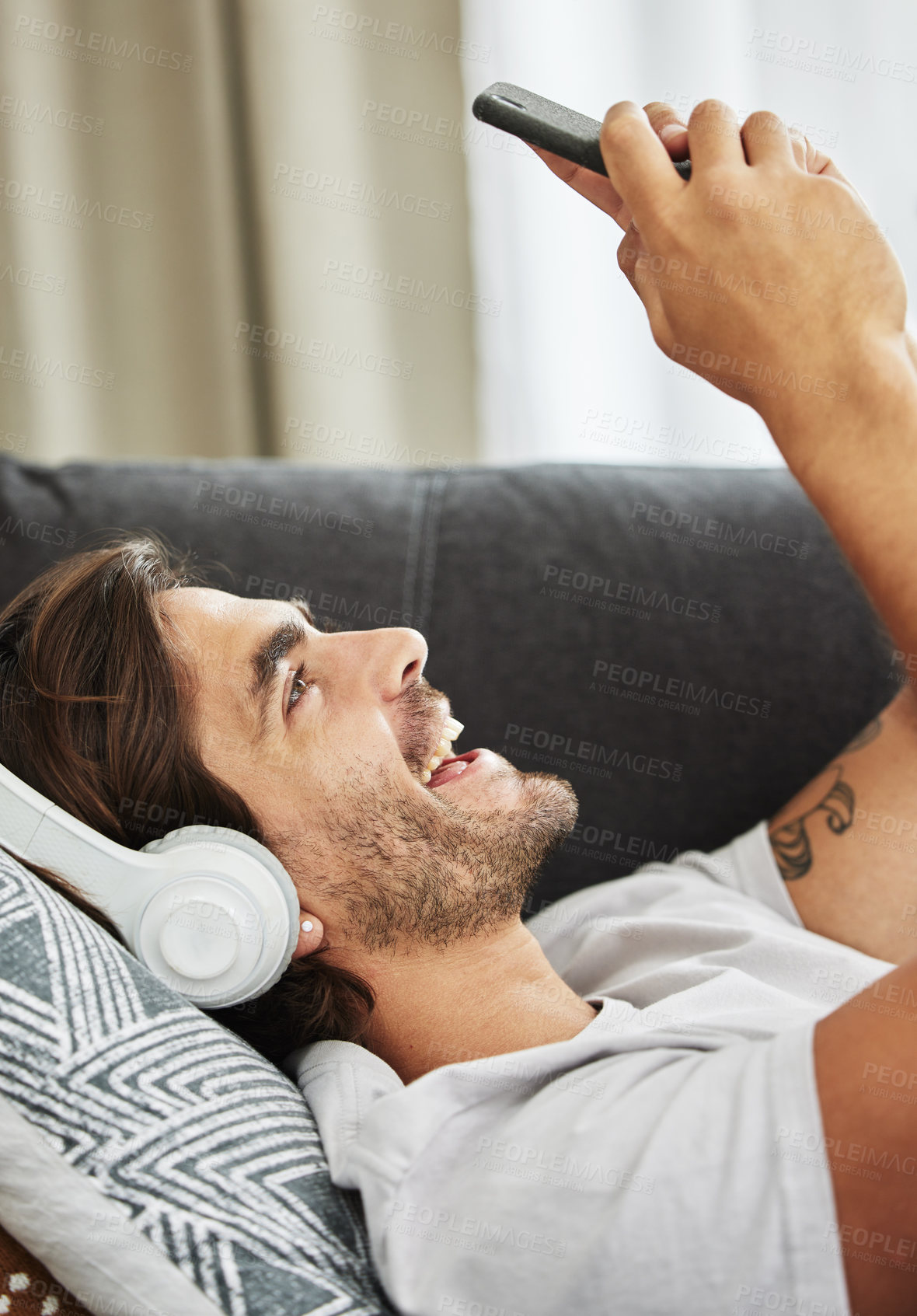 Buy stock photo Man, headphones and phone for sound on couch, relax and listen to song and scroll on social media. Male person, home and rest app for playlist or conversation, text and podcast audio for streaming