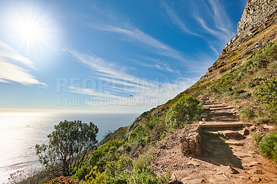 Buy stock photo Copy space with scenic coast and rocky mountain slope with cloudy blue sky background. Rugged landscape of plants growing on a cliff by the sea with hiking trails to explore in Cape Town South Africa