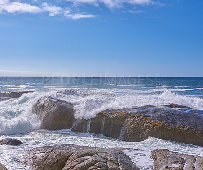 Buy stock photo Rocks in the ocean under a cloudy blue sky with copy space. Scenic landscape of beach waves splashing against boulders or big stones in the sea at a popular summer location in Cape Town, South Africa