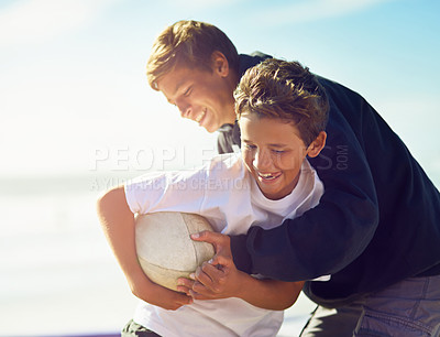 Buy stock photo Shot of two happy brothers playing with a rugby ball on the beach