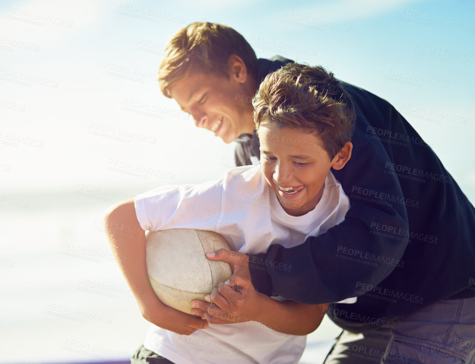 Buy stock photo Shot of two happy brothers playing with a rugby ball on the beach