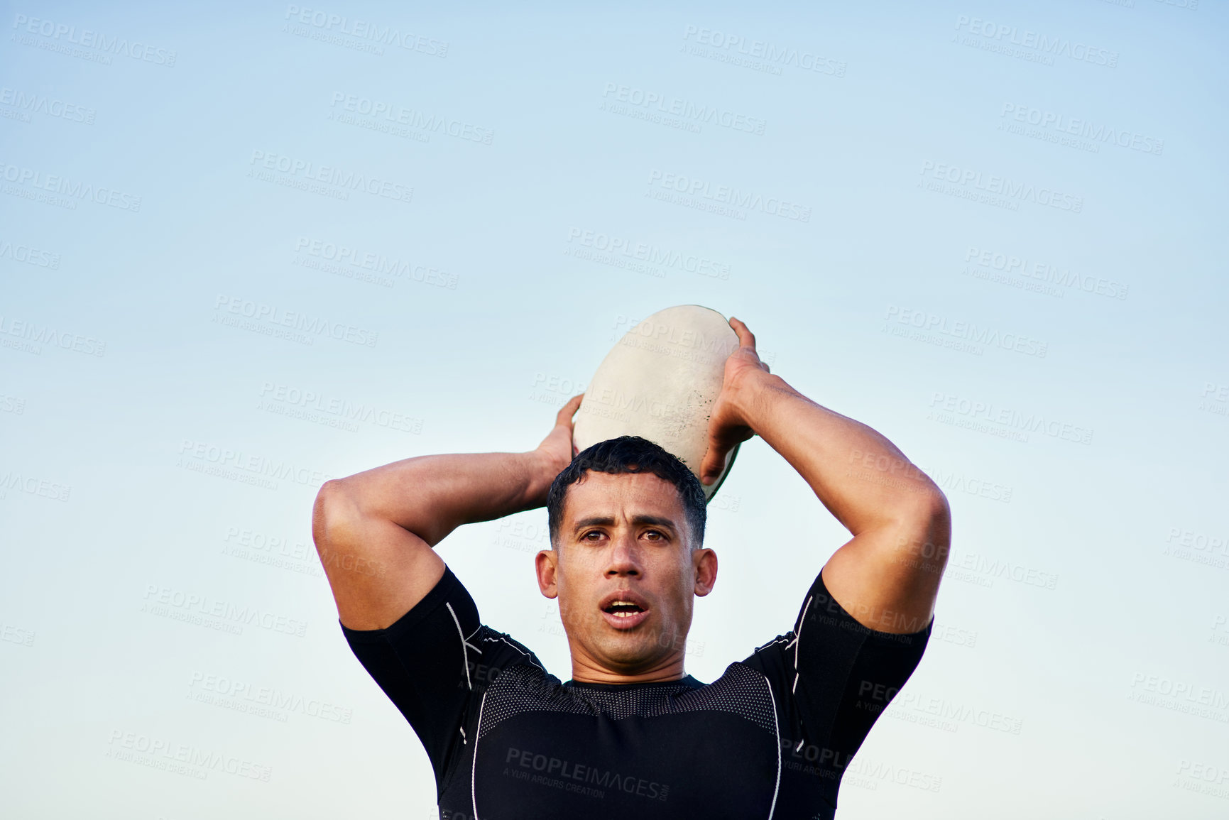 Buy stock photo Cropped shot of a handsome young sportsman standing alone and throwing a rugby ball during practice during the day
