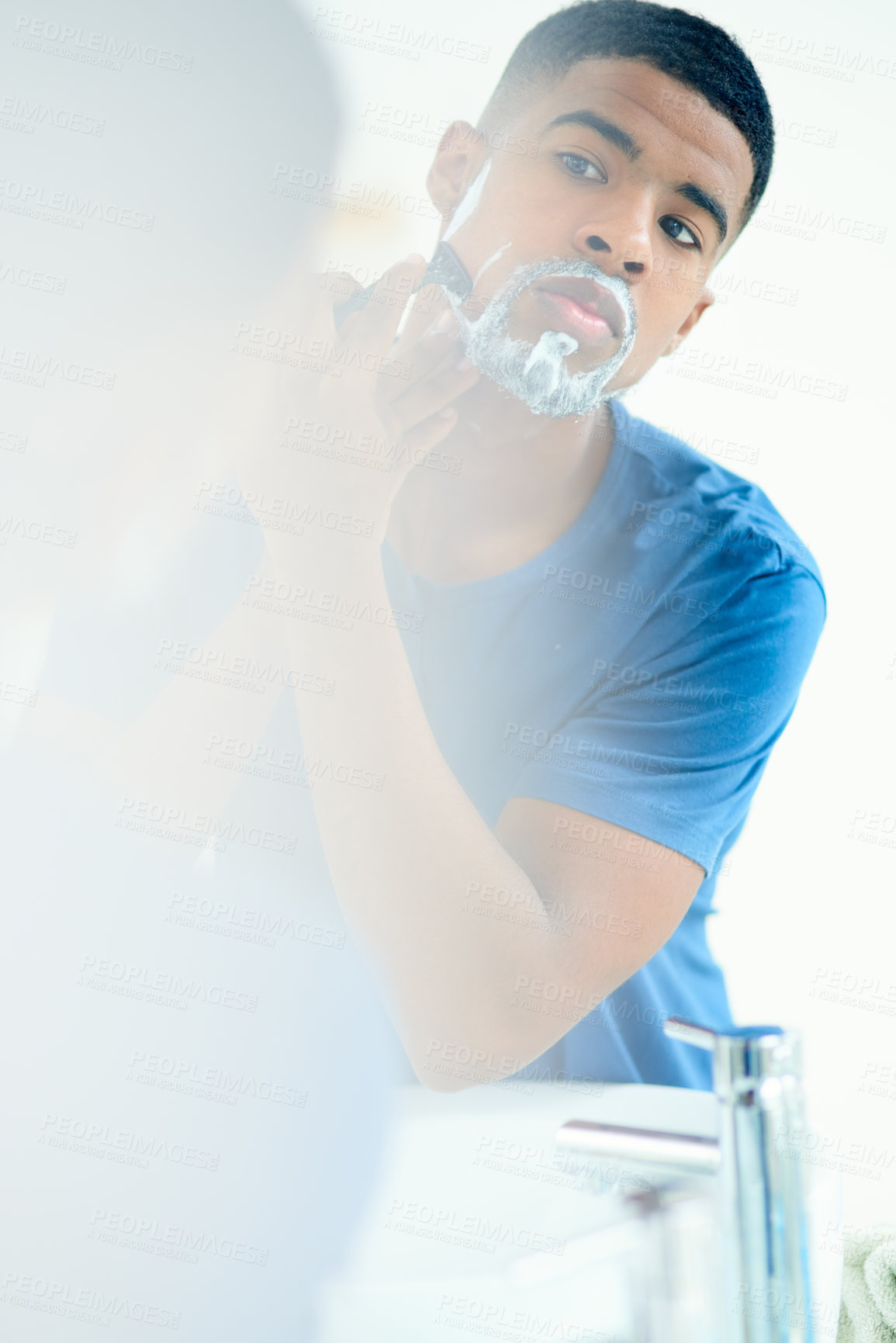 Buy stock photo Shot of young man shaving his face in his bathroom mirror