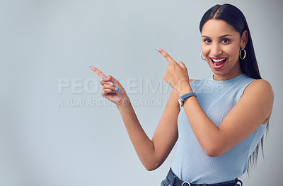 Buy stock photo Cropped portrait of an attractive young woman gesturing towards copyspace while standing against a grey background in studio