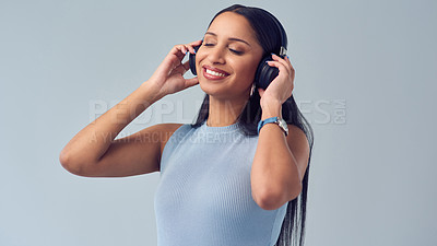 Buy stock photo Cropped shot of an attractive young woman listening to music while standing against a grey background in studio