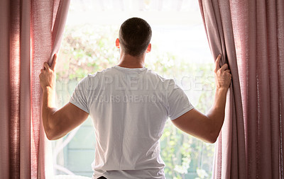 Buy stock photo Shot of a young man opening his curtains to a bright sunny morning