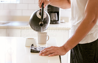 Buy stock photo Making a cup of breakfast tea early in the morning. One person preparing a mug of coffee to drink early in the morning in the kitchen. Male making a warm beverage while holding a kettle with water