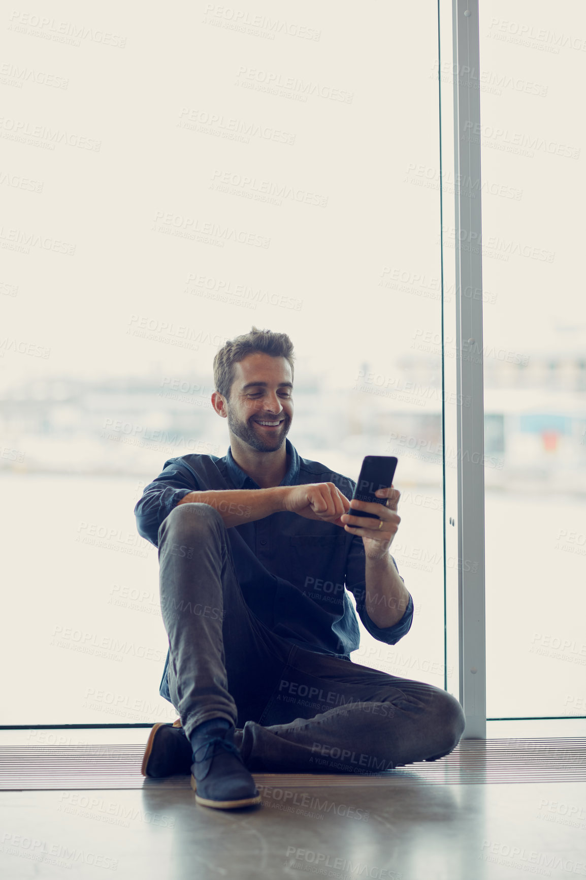 Buy stock photo Full length shot of a handsome young businessman sitting alone in an airport terminal and using his cellphone